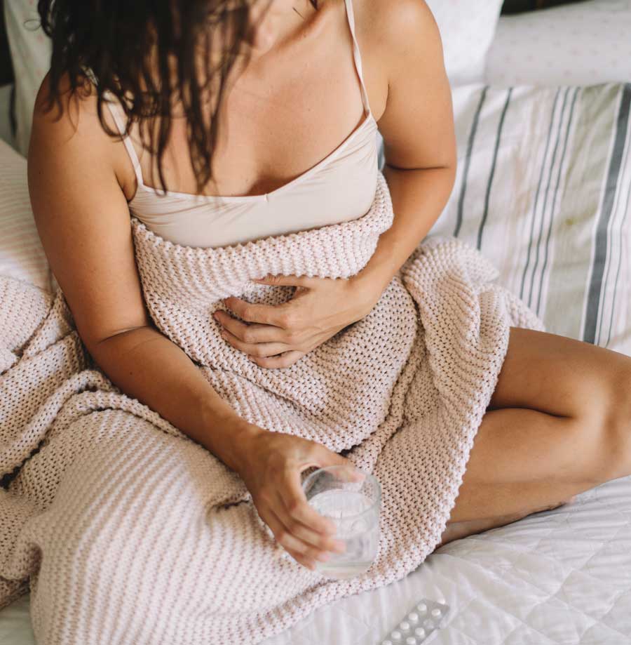 Woman sitting in the bed with a glass of water and aspirin | Acupuncture for Menstrual Cramps and PMS
